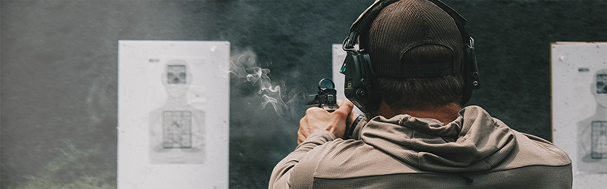 Shooter firing a pistol at a paper target, with smoke from the shot